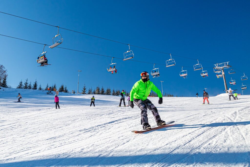 Snowboardzista zjeżdżający po stoku w Bałtowie, nad nim czteroosobowa kolej krzesełkowa