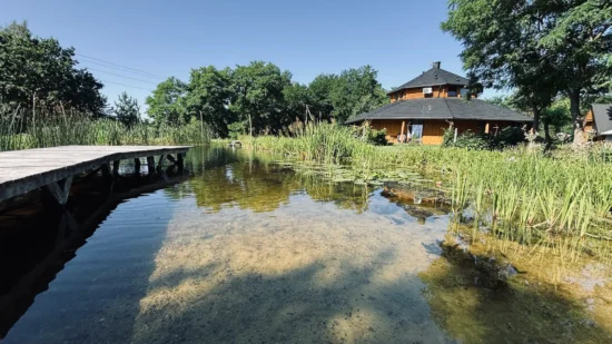 Basen naturalny 26 na 13 metrów z drewnianym pomostem i ośmiokątnym domem ze słomy w tle, agroturystyka Złoty Klon w Kijance