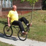 Józef Majewski jedzie na rowerze poziomym przed muzeum w Gołębiu