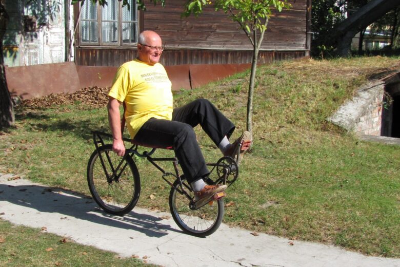 Józef Majewski jedzie na rowerze poziomym przed muzeum w Gołębiu