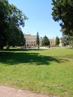 Pałac Czartoryskich w Puławach widziany przez parkowy trawnik, po bokach stare drzewa