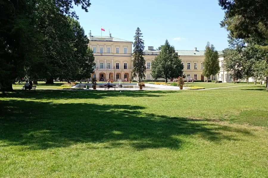 Pałac Czartoryskich w Puławach widziany przez parkowy trawnik, po bokach stare drzewa